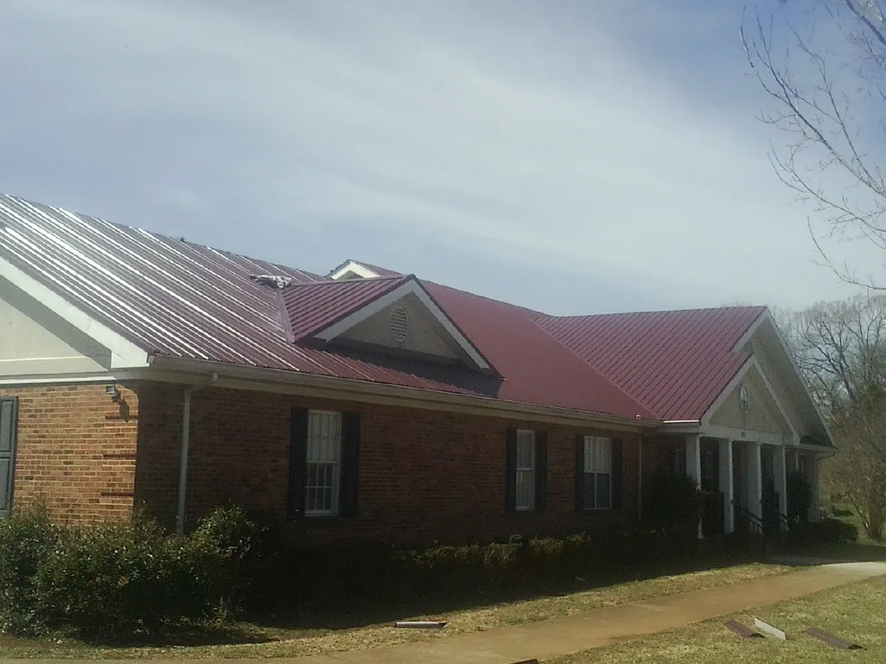 Red metal roof with gabled entries on a long brick building, from a Hail Damage Roof Repair job in Corte Madera