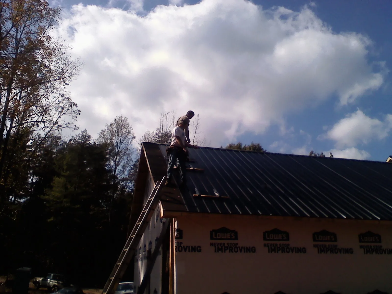 Roofer fastening dark metal panels high against a cloudy sky, from a Roof Inspection job in Corte Madera